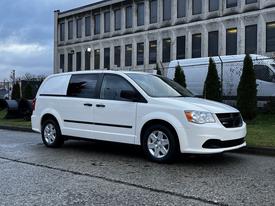 A white 2012 RAM Cargo van with a sleek design features sliding side doors and chrome wheels parked on a road