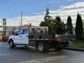 A white 2017 Ford F-350 SD pickup truck with a flatbed carrying potted palm trees and equipped with a tool box on the side