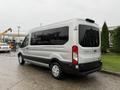 A silver 2019 Ford Transit van parked with its back door visible featuring large windows and a black lower body near the rear wheels