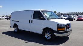 A white 2012 GMC Savana van parked in a lot with its side doors closed and a simple design featuring headlights and wheels visible