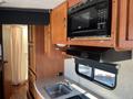 Interior view of a 2012 Ford Econoline showing a kitchen area with wooden cabinets a microwave sink and a stove