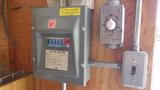 A gray electrical control panel with various switches and a timer dial mounted on a wooden wall