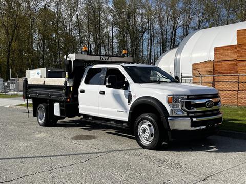 2021 Ford F-550 truck in white with a flatbed and tool boxes on the sides parked on a paved surface