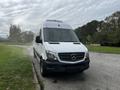 A 2016 Mercedes-Benz Sprinter van with a white exterior and black grille parked on a road with smoke emanating from the exhaust