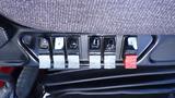 Five toggle switches on a panel labeled with seat symbols in black and gray colors with one red switch