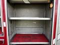 The interior compartment of a 1994 Freightliner FL80 featuring two metal shelves with a textured red floor and a light fixture on the side