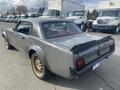 A 1966 Ford Mustang with a sleek silver body and gold wheels is parked, showcasing its classic design and sporty rear end