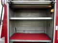 Interior of a 1994 Freightliner FL80 storage compartment featuring metal shelves and a red rubber floor mat
