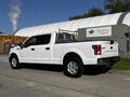 A white 2017 Ford F-150 truck with a silver rack on the bed is parked at an angle showing the driver's side and rear of the vehicle