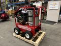 A red Magnum 4000 Hot Water Pressure Washer on a wooden pallet featuring large wheels a stainless steel tank and various hoses and controls