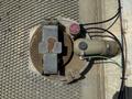 A circular metal access cover with a rusted latch mechanism and a connected hose featuring a pressure regulator with visible labels