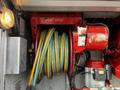 A coiled yellow and blue hose on a red reel with knobs and switches attached to a 1994 Freightliner FL80