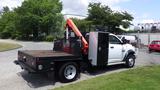 A 2014 RAM 5500 flatbed truck with a crane attachment on the rear and a black bed is parked on a residential street