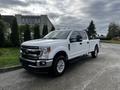 A white 2020 Ford F-250 SD pickup truck with chrome accents and a spacious cab parked on a gravel surface