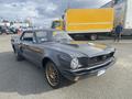 A 1966 Ford Mustang in a sleek gray color with black accents and gold alloy wheels parked with its distinctive grille and headlights prominently displayed