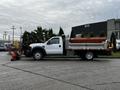 A 2009 Ford F-550 truck with a plow attached in front and a flatbed with sides at the rear