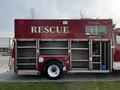 A red 1994 Freightliner FL80 rescue truck with open compartments and the word "RESCUE" displayed prominently on its side