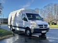 A 2008 Dodge Sprinter Van with a white exterior and a high roof parked on a wet surface with shadows visible on its side