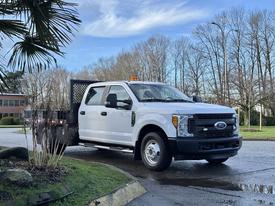 A 2017 Ford F-350 SD truck with a flatbed and an orange light on the roof parked on a driveway