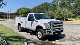 A white 2015 Ford F-350 SD Service Truck with an open bed and toolbox attached to the side parked on a paved area