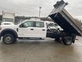 A white 2021 Ford F-550 truck with a raised dump bed showcasing a flatbed design and visible wheels on either side