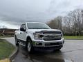 A white 2018 Ford F-150 pickup truck with a chrome grille and alloy wheels positioned at an angle on a street