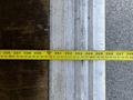 A yellow measuring tape laid flat across metal and wood surfaces with marked measurements visible