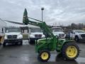 A green 2003 John Deere 790 tractor with a front loader attachment parked in a lot with white trucks in the background