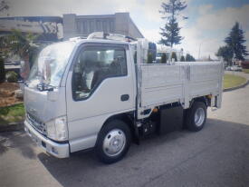 A silver 2008 Isuzu Elf truck with a flatbed and side panels parked on a street