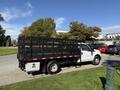 A 2016 Ford F-350 SD truck with a black flatbed and metal railing system parked on a street