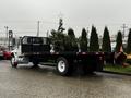 A 2011 International DuraStar 4300 flatbed truck with a black bed and a white cab parked on a wet surface