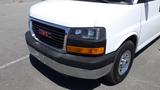 A white 2012 GMC Savana van with a silver bumper and chrome wheel covers featuring a black grille and orange headlights