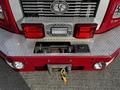 The rear of a red 1994 Freightliner FL80 featuring chrome accents a metal bumper and a diamond plate surface with tools and equipment housed beneath the rear lights