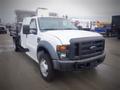 A 2008 Ford F-550 with a white cab and black front grille as well as dual rear wheels and a flatbed attachment