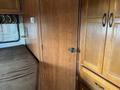 A 2012 Ford Econoline interior featuring wooden cabinetry and a bed against a wall with a door and small appliances