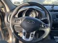 Steering wheel of a 2012 Kia Sportage with control buttons and the Kia logo in the center