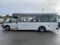 A 2018 Chevrolet Express bus with a white body and large windows parked on a wet surface