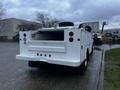 A white 2014 Ford F-350 SD truck with a flatbed and dual rear wheels viewed from the back