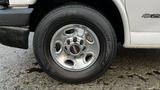 A close-up of a shiny chrome wheel of a 2005 Chevrolet Express featuring a black and red GMC logo and Kumho tires with visible tread pattern