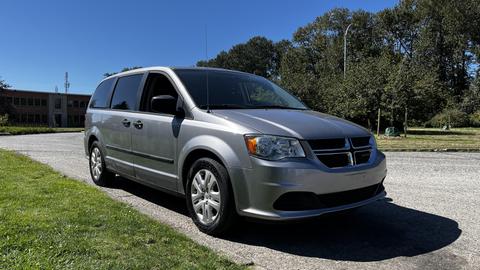 A silver 2016 Dodge Grand Caravan parked on a paved area with trees in the background