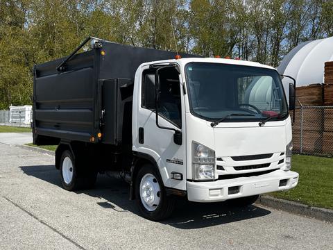 A 2016 Isuzu NPR light-duty truck with a white cab and a black dump bed parked at an angle with the front facing the viewer