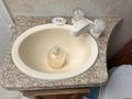 A beige sink with a round bowl and a soap dispenser sits on a speckled countertop next to two decorative glass candle holders