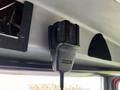 A black microphone attached to the interior of a vehicle's ceiling, with a textured surface and a coiled cable connected to it