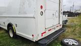 A white 2006 Ford Econoline with a cargo area and a rear loading door parked on grass next to a tire