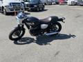 A 2019 Kawasaki W800 CAFÉ motorcycle with a black and silver design featuring a retro style round headlight and a brown seat positioned on a paved surface