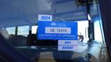 A blue and white sticker on the window of a 2014 International 3000 bus indicating a certificate of approval for British Columbia with dates for July and August 2024