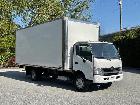 A 2020 Hino 195 box truck with a white exterior and a large cargo area on the back is parked with the driver's side facing forward