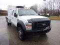 A white 2009 Ford F-450 SD truck with a flatbed and tools in the back featuring a black grill and wheel covers