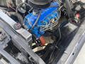 A detailed view of a 1966 Ford Mustang engine showing a blue engine block with various hoses and components visible