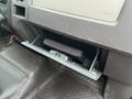 A partially opened glove compartment of a 2010 Ford F-150 containing a black item inside